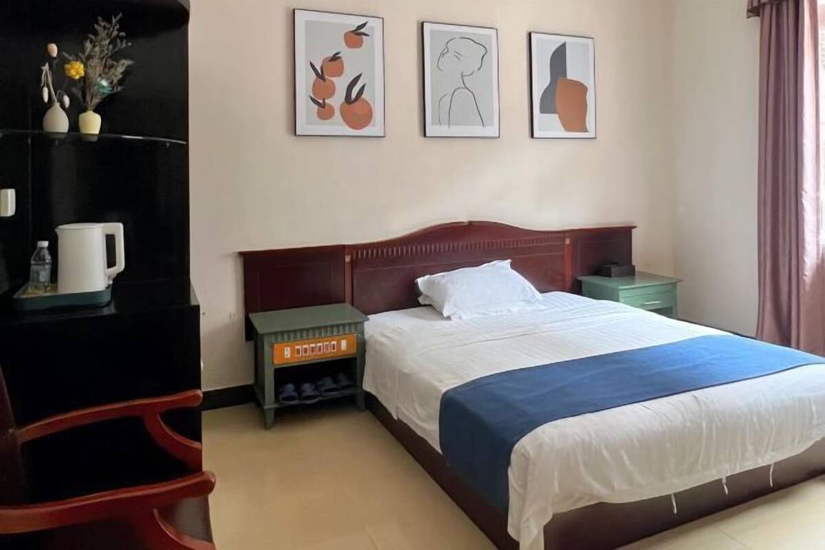 A hotel room with a bed, a desk, a nightstand, and three framed pictures on the wall.