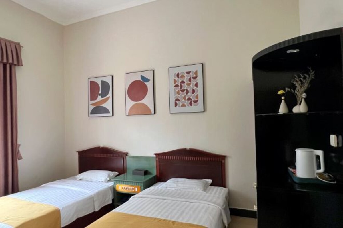 Habitación de hotel con dos camas individuales, un escritorio, una silla y un mueble negro con una taza blanca.
