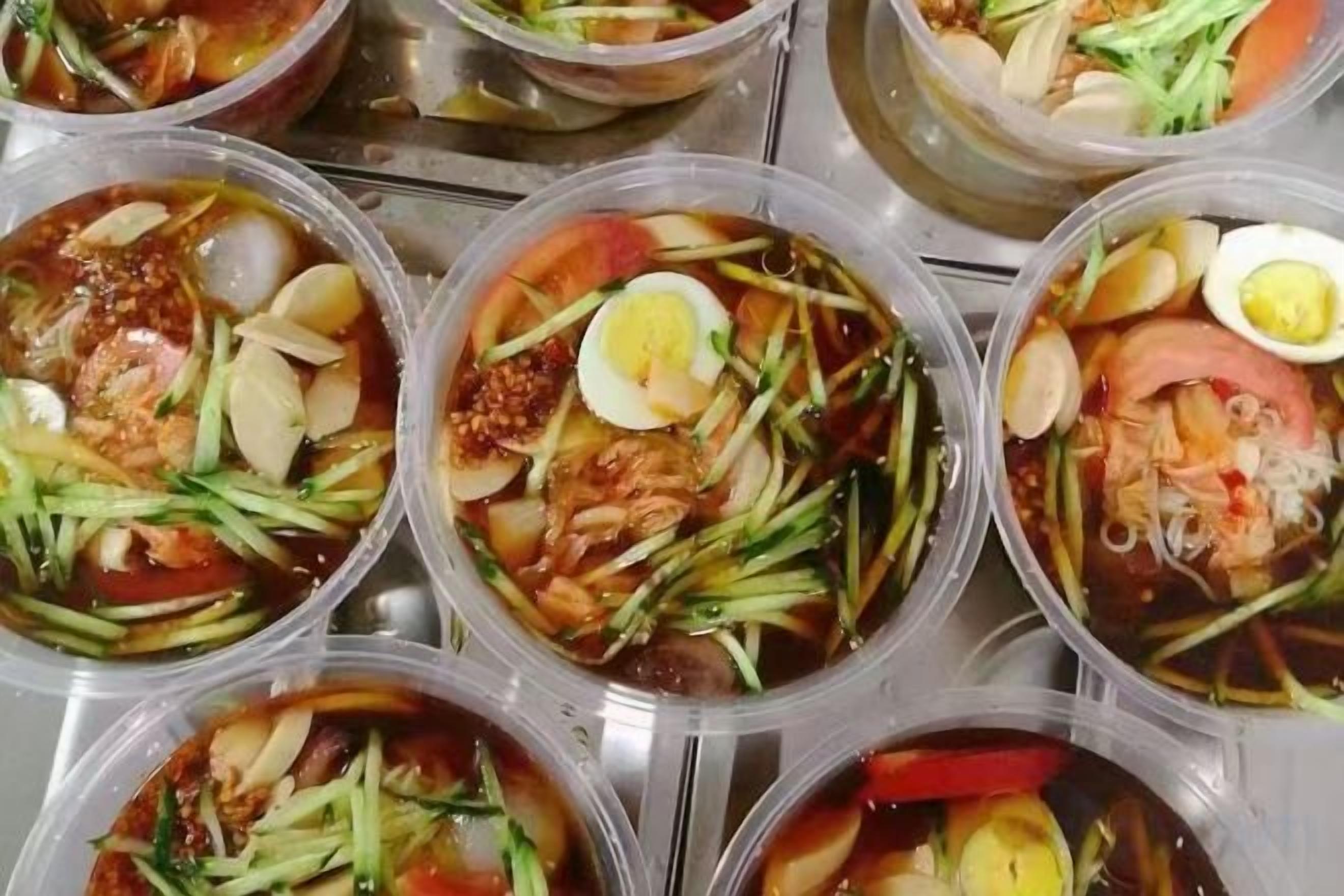 Plusieurs portions d’un plat agrémenté de divers accompagnements, notamment des œufs et des légumes, présentées dans des récipients en plastique transparent.