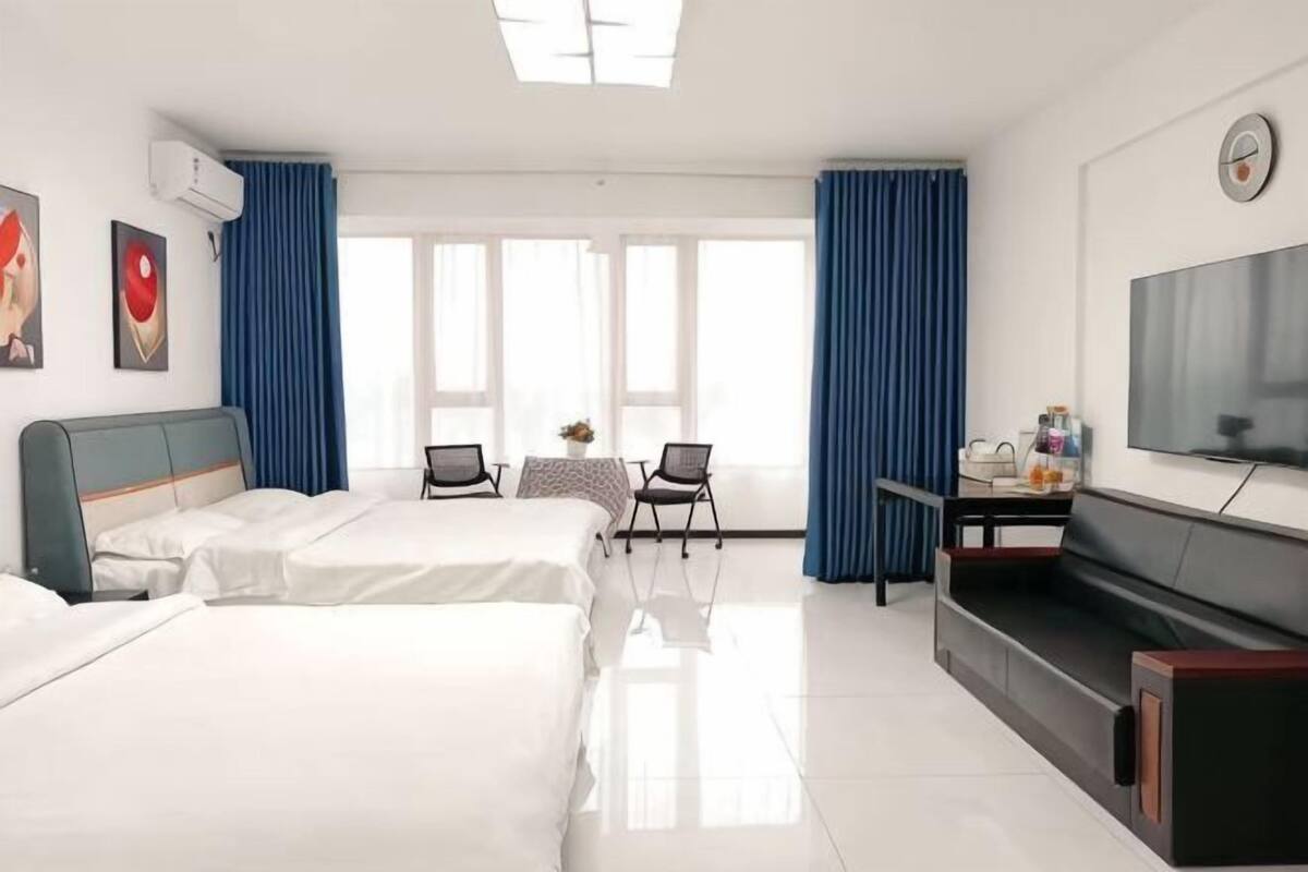 A hotel room with two beds, a TV, a desk with a chair, and a window with curtains.