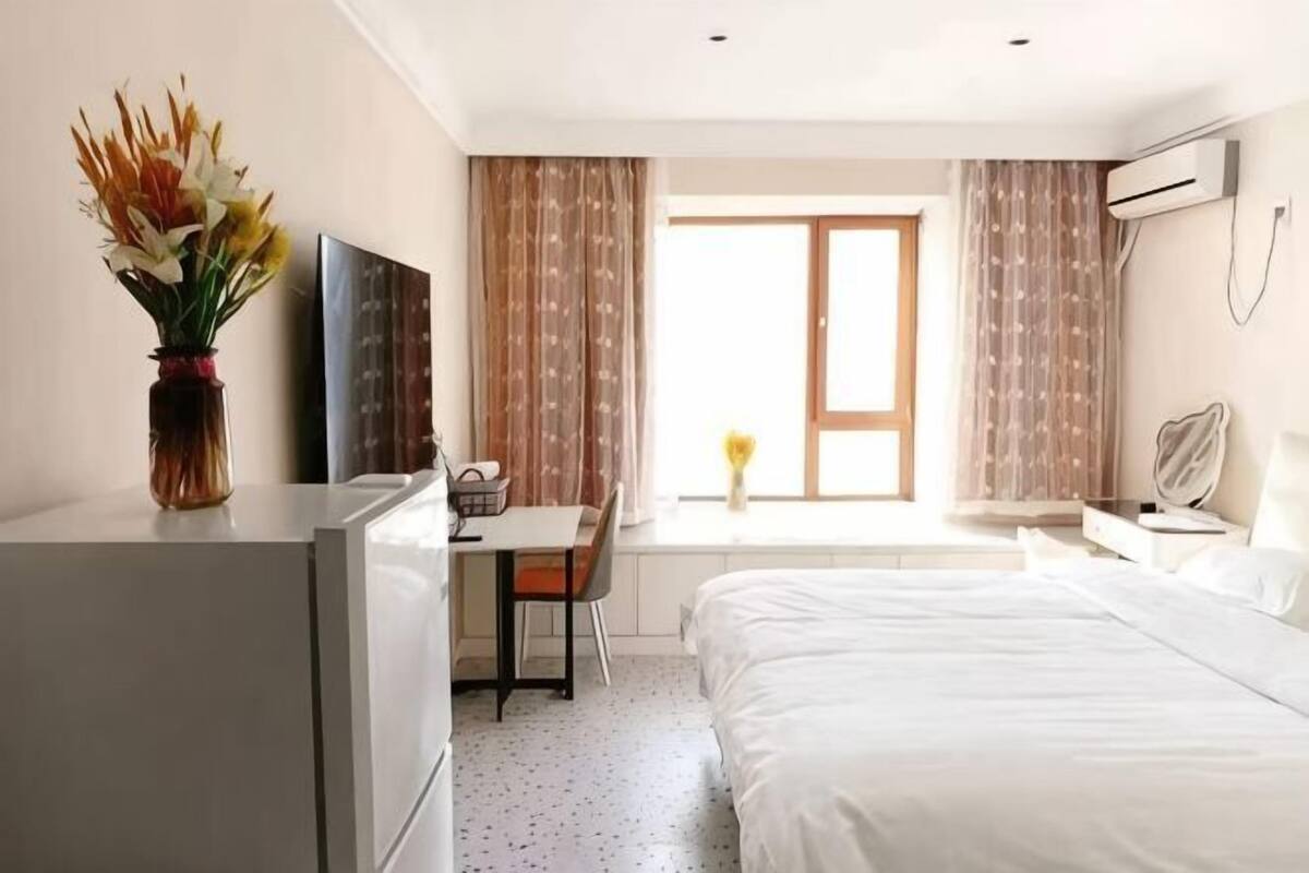 A hotel room with a bed, a desk, a chair, a TV, and a window with curtains.