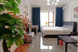Habitación de hotel con cama, escritorio, silla, mesa, planta y ventana con cortinas.