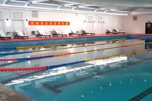 A swimming pool with lane dividers and a tiled floor, surrounded by lounge chairs and a red and white wall. - Century Hongyuan Hotel (Chongqing Road Branch) (Changchun)
