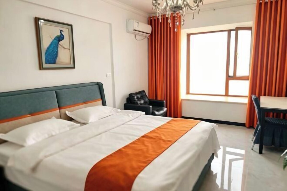 Ein Hotelzimmer mit einem Bett, einem Schreibtisch, einem Stuhl, einem Pfauenbild und einem Fenster mit Vorhängen.
