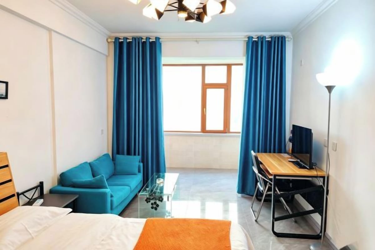 A hotel room with a bed, a sofa, a desk, and a window with curtains.