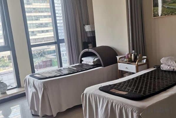 A hotel room with two beds, a window with curtains, a nightstand with a lamp, and a view of the city.
