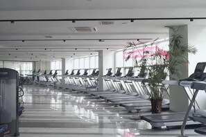 Une salle de sport avec des tapis de course alignés en rangées, un vélo d’appartement et une plante en pot.