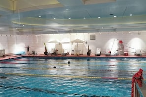 Ein Hallenbad mit Bahnen, Liegestühlen und einem Rettungsschwimmerstand.