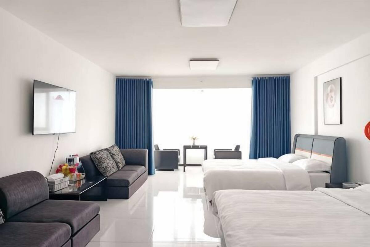 A hotel room with a sofa, two beds, a TV, and a view of the outdoors.