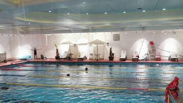 An indoor swimming pool with lanes, lounge chairs, and a lifeguard stand.