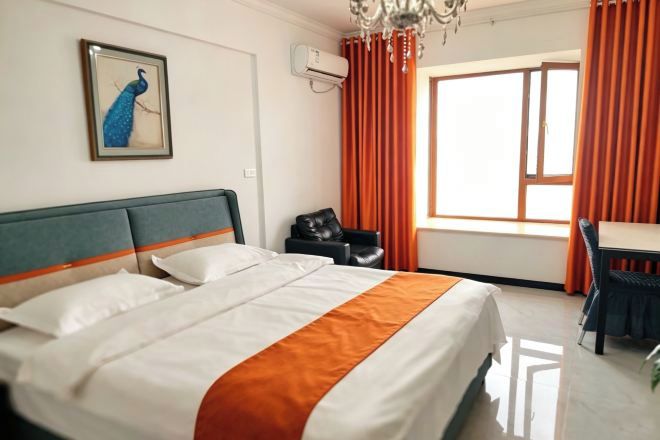 A hotel room with a bed, a desk, a chair, a peacock painting, and a window with curtains.