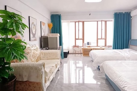 A hotel room with a sofa, a desk, two beds, a TV, and a large window with curtains.