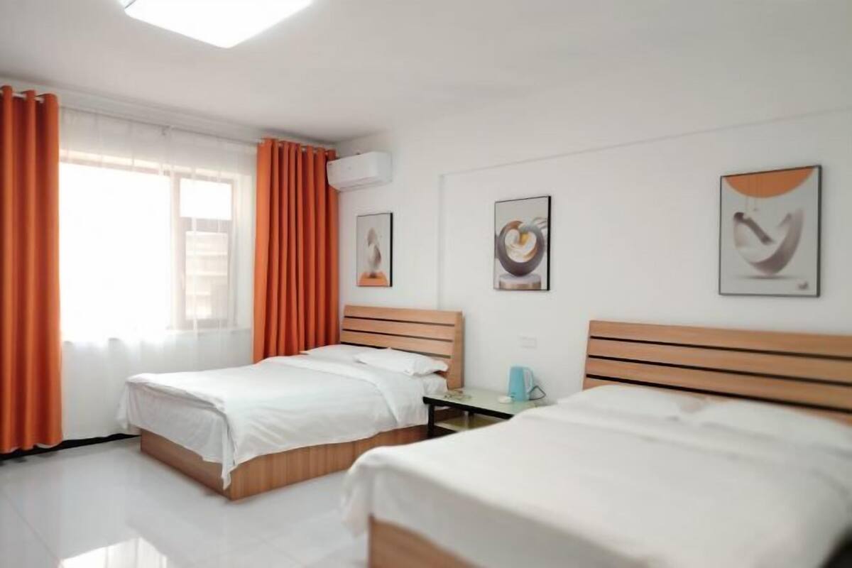 A hotel room with two beds, a window with curtains, an air conditioning unit, and artwork on the walls.