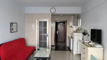 Een gezellig, compacte leefruimte met een rode bank, een klein tafeltje, een televisie en een kitchenette.