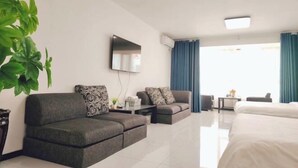 Et moderne hotelværelse med sofa, seng, fjernsyn og et stort vindue med gardiner.