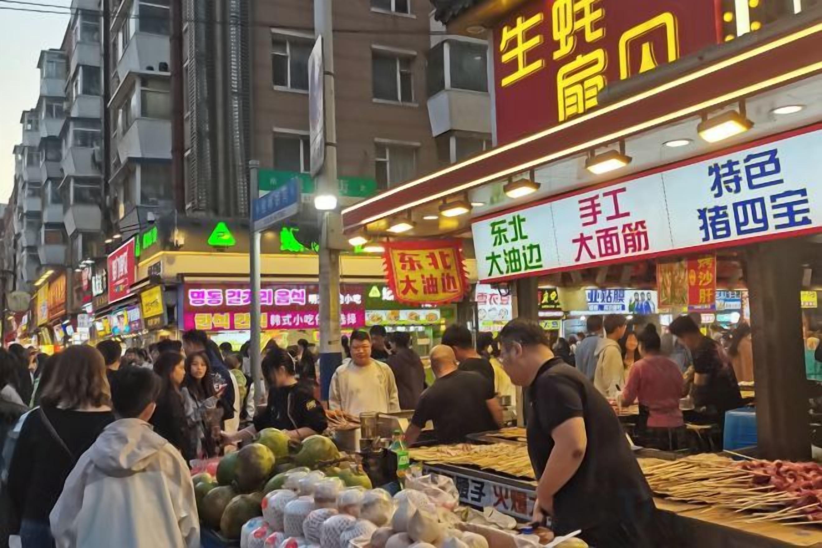 A bustling street market with various stalls and signs, indicating a variety of goods and services available.