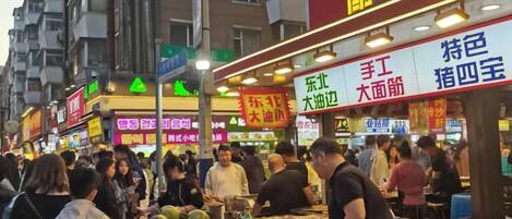 A bustling street market with various stalls and signs, indicating a variety of goods and services available.