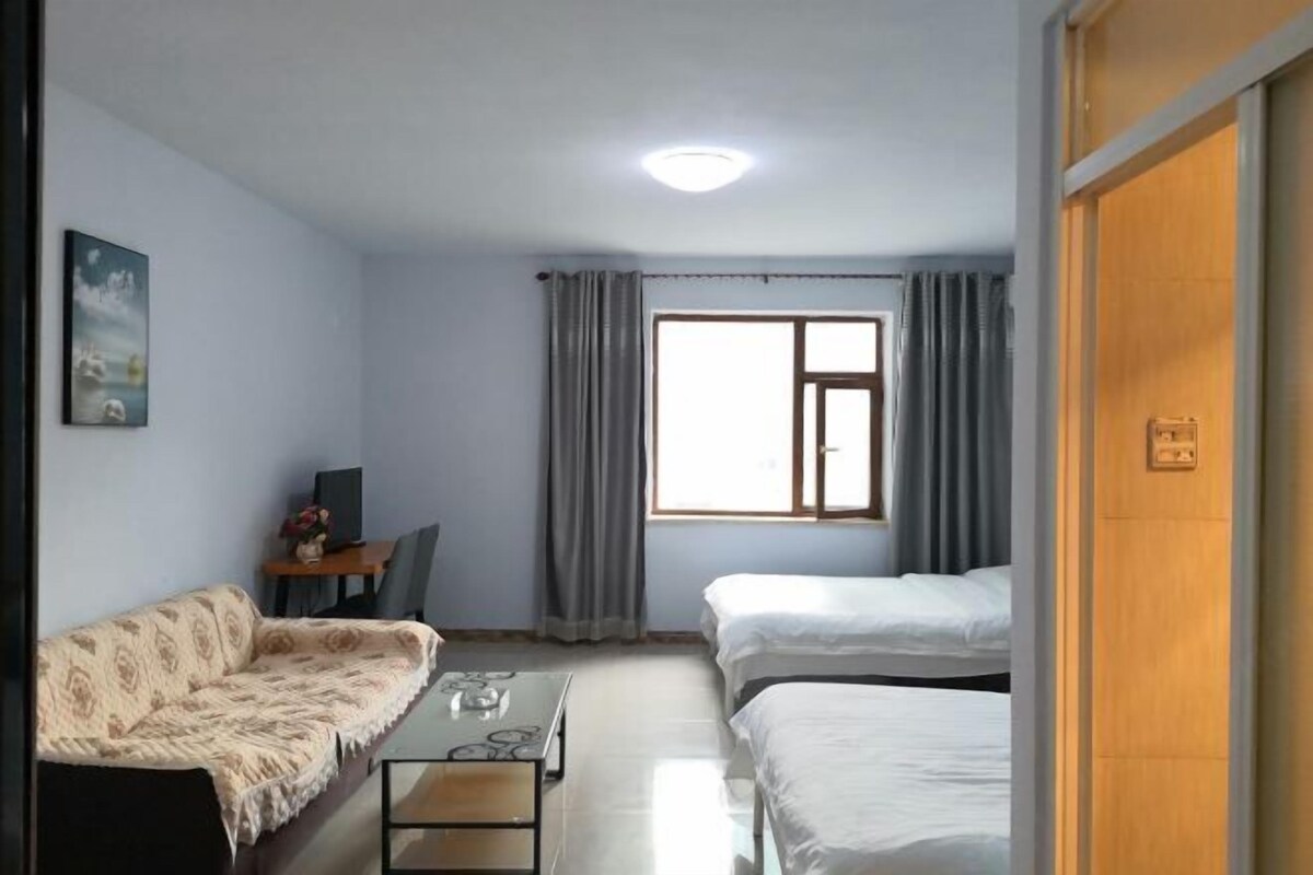Ein Hotelzimmer mit einer Couch, zwei Einzelbetten, einem Schreibtisch mit Stuhl und einem Fenster mit Vorhängen.