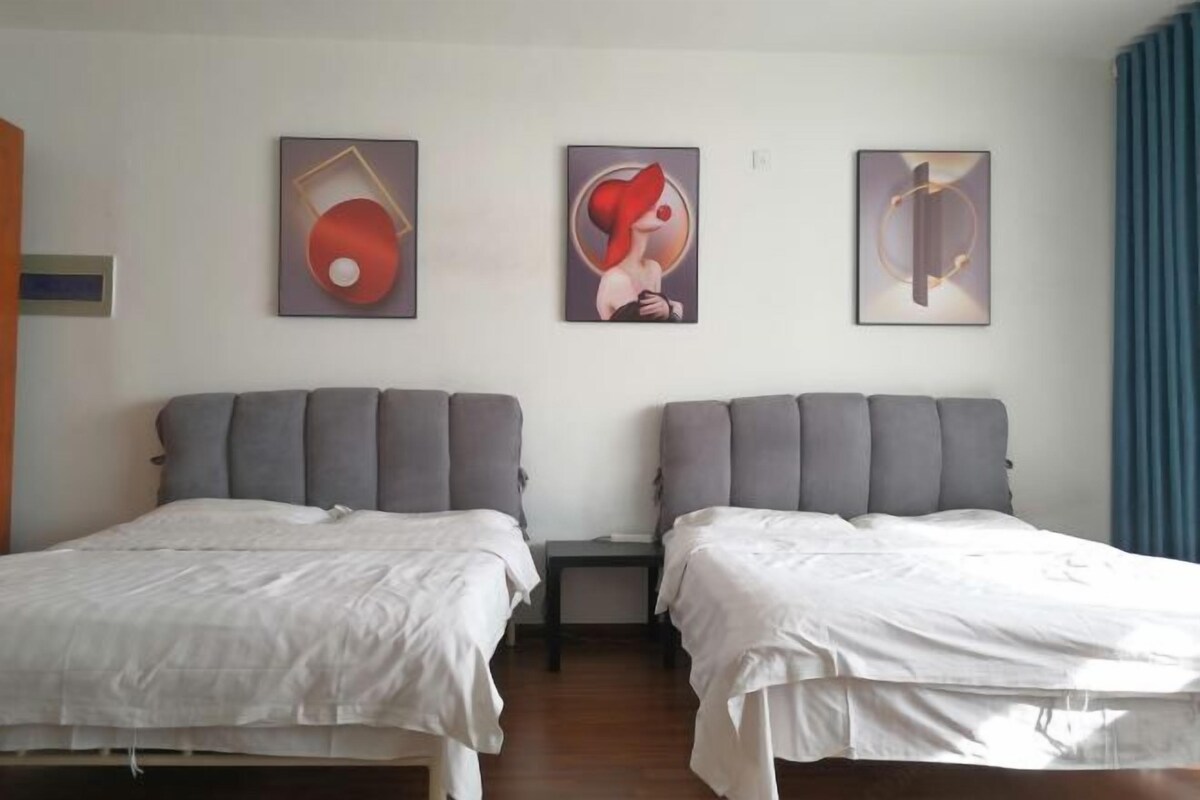 Ein Hotelzimmer mit zwei Betten, beide mit grauen Kopfteilen und weißer Bettwäsche. An der Wand hängen drei gerahmte Kunstwerke.