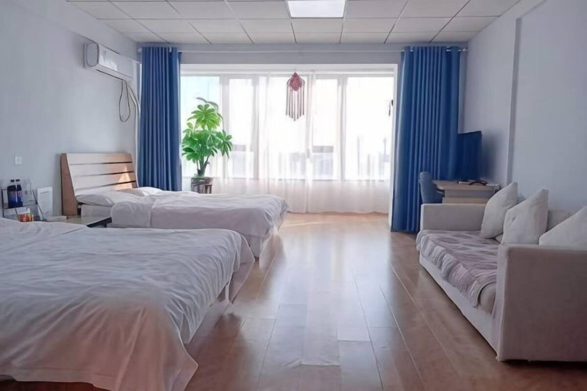 A hotel room with two beds, a sofa, a TV, a plant, and a large window with curtains.