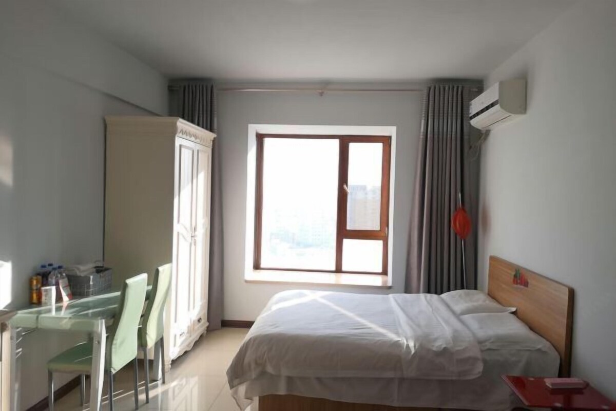 Ein Hotelzimmer mit einem Bett, einem Schreibtisch mit Stühlen, einem Fenster mit Vorhängen und einer Klimaanlage.