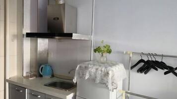 Een keuken met een roestvrijstalen afzuigkap, een spoelbak, kasten en een kleine tafel met een vaas en een waterkoker.