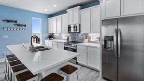 A modern kitchen with white cabinets, stainless steel appliances, a central island with stools, and a blue accent wall. - Fishy Business| Beach Front Oasis!  Sleeps 20! (Bolivar Peninsula)