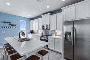 Una cocina moderna con armarios blancos, electrodomésticos de acero inoxidable, una isla central con taburetes y una pared de acento azul.