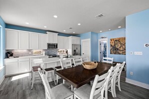 A modern kitchen with white cabinets, a dark wooden dining table, and a blue accent wall. - Fishy Business| Beach Front Oasis!  Sleeps 20! (Bolivar Peninsula)