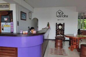 A reception area with a purple counter, a wooden clock, and a table with a coffee machine. - Erawan Place (Mae Sot)