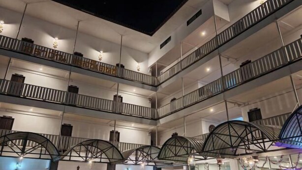 Un hôtel à plusieurs niveaux, avec un intérieur comprenant des balcons, des luminaires suspendus et un atrium central orné d’arches.