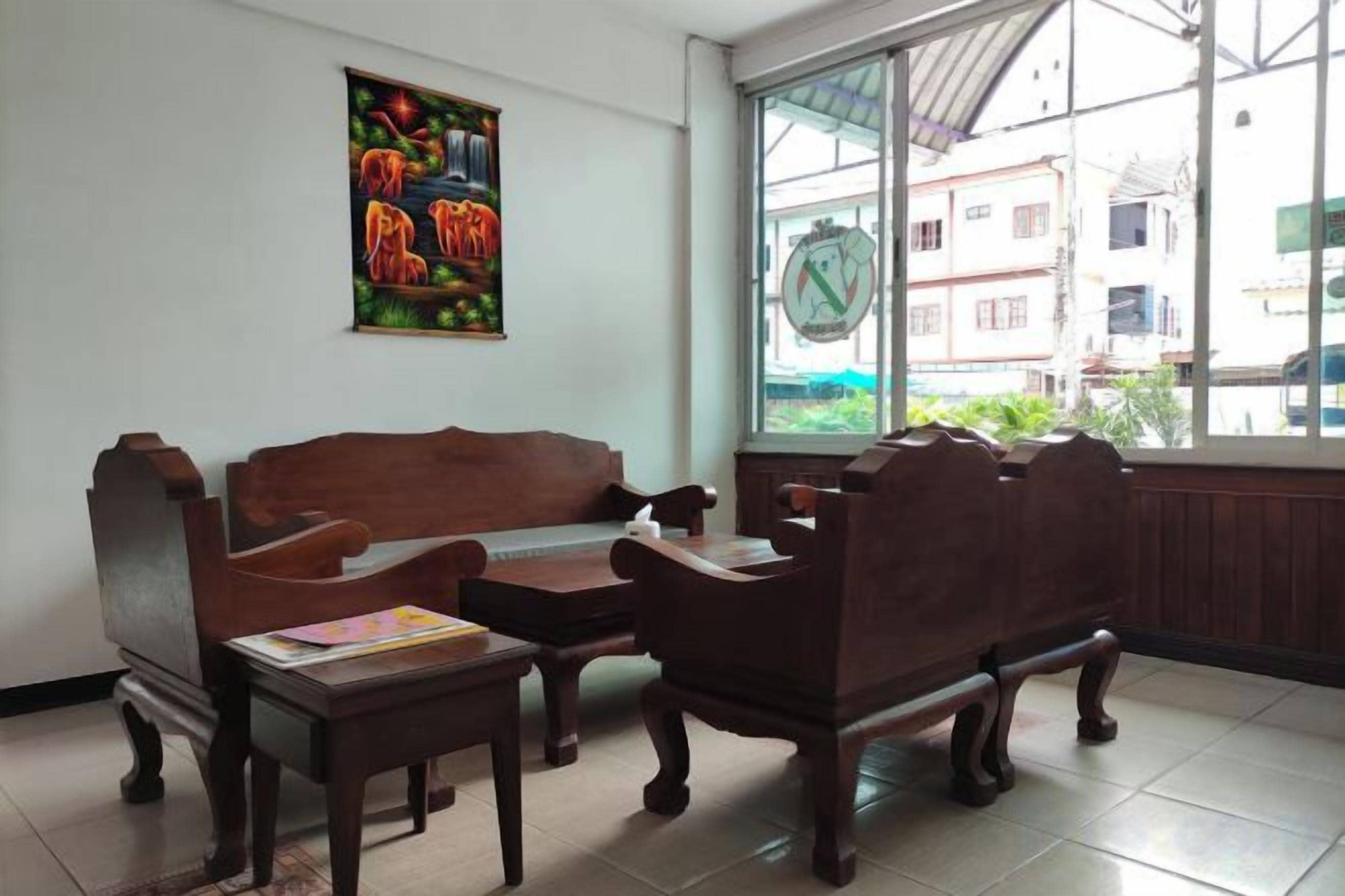 A room with a wooden sofa and two chairs, a small table, a window with a view of buildings, and a colorful poster on the wall.