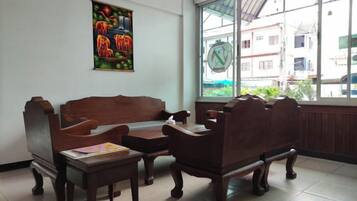 A room with a wooden sofa and two chairs, a small table, a window with a view of buildings, and a colorful poster on the wall.