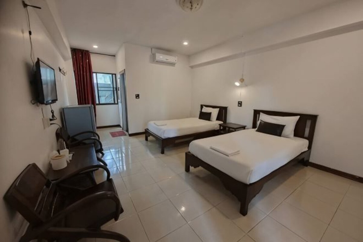 A hotel room with two beds, a desk, a chair, a TV, and an air conditioning unit.
