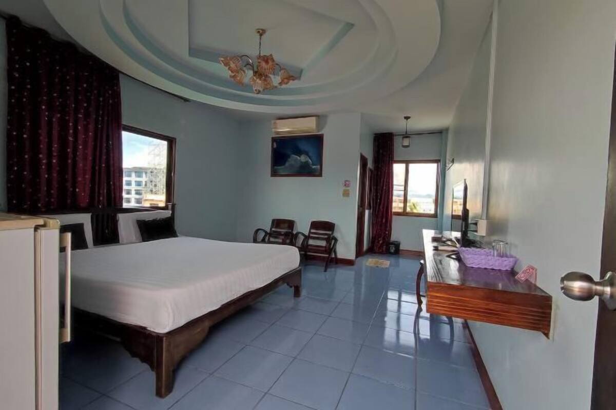 A hotel room with a bed, chairs, a desk, a mirror, and a view of the city.