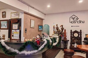 A reception area with a wooden counter, a clock, and various decorative items. - Erawan Place (Mae Sot)