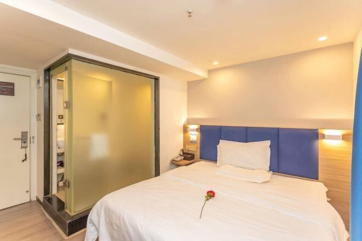 A hotel room with a bed, a nightstand, a wall-mounted lamp, and a door with a frosted glass panel.
