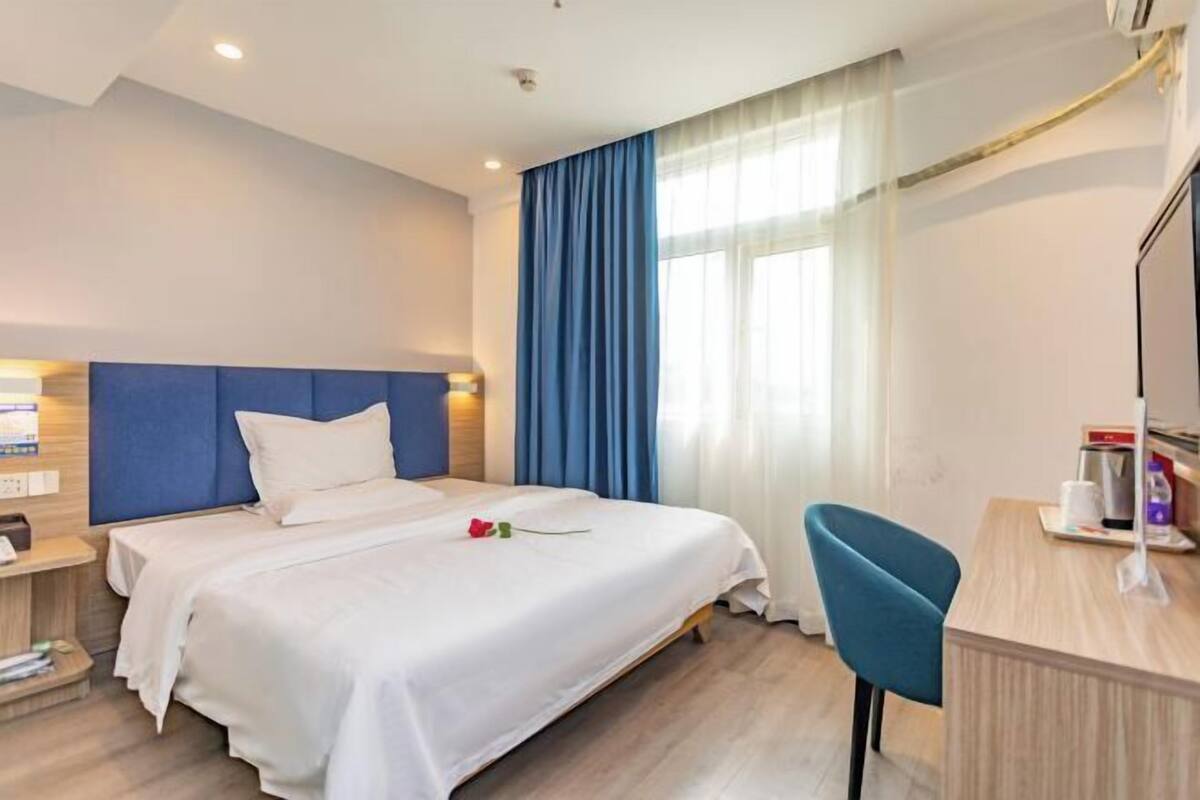 A hotel room with a bed, a desk, a chair, and a window with curtains.