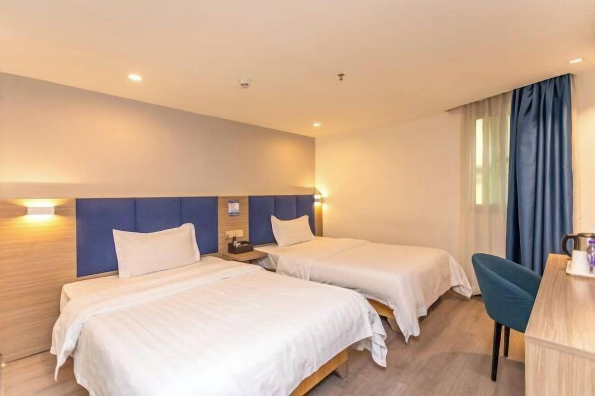 A hotel room with two beds, a desk, and a window with curtains.