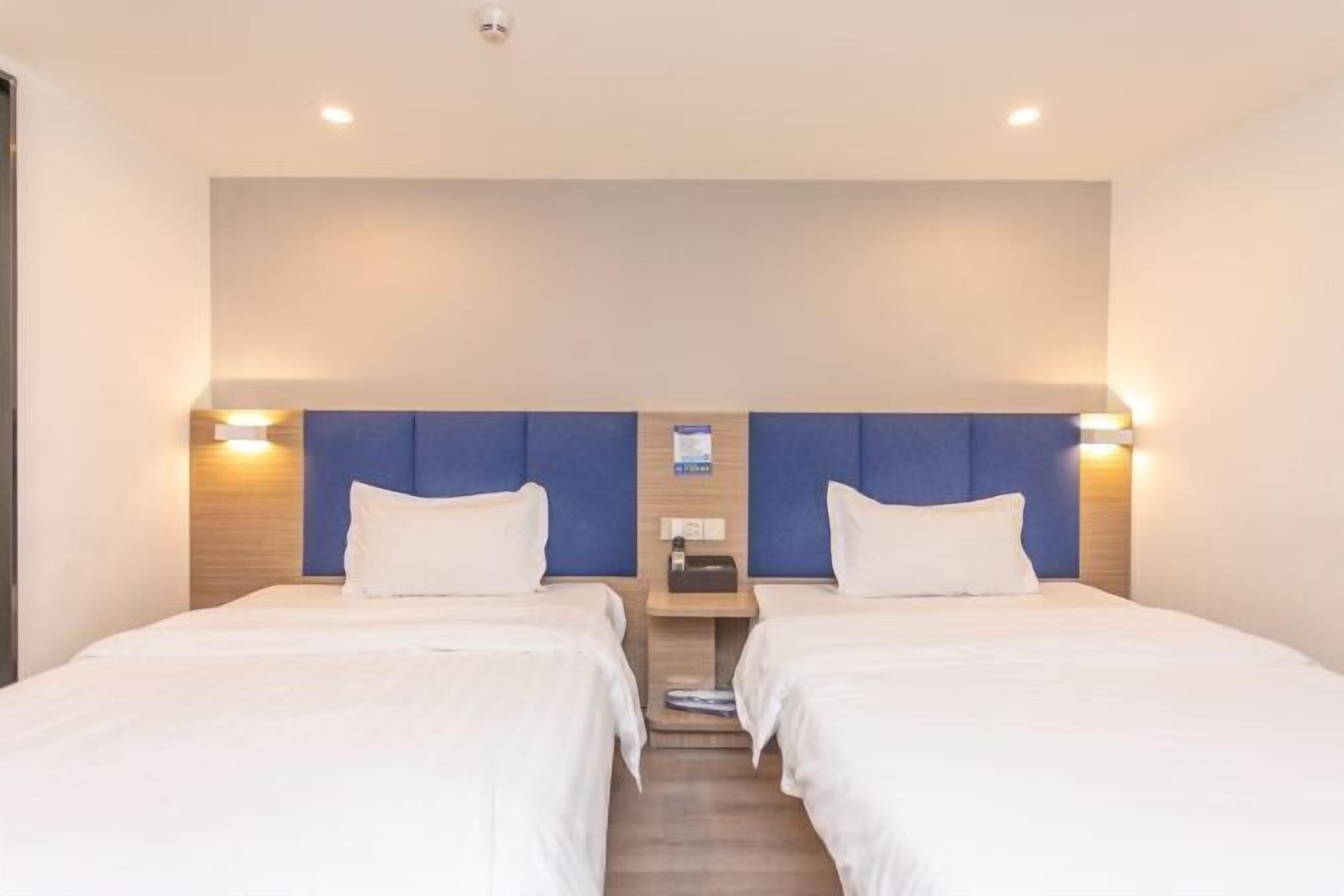 A hotel room with two beds, a wooden headboard, a nightstand, and a wall-mounted charging station.