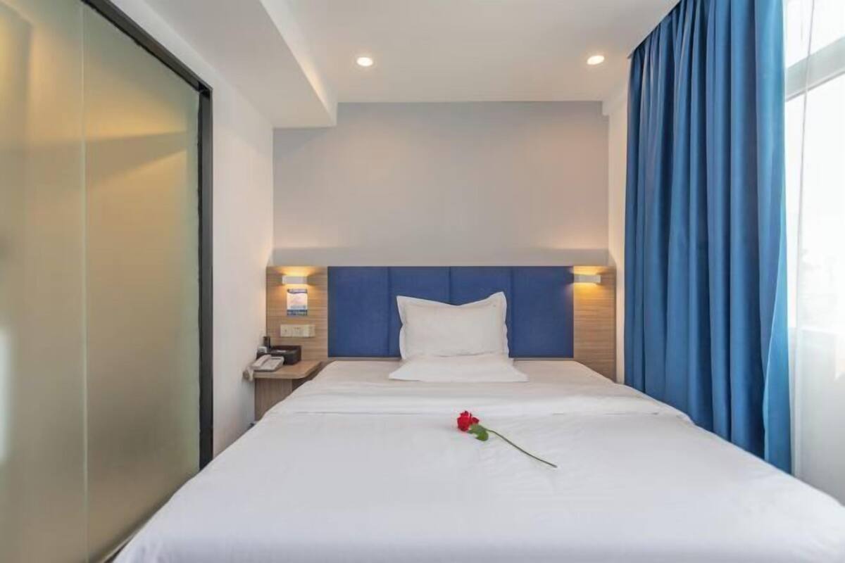 A hotel room with a bed, a nightstand, a phone, and a window with curtains.