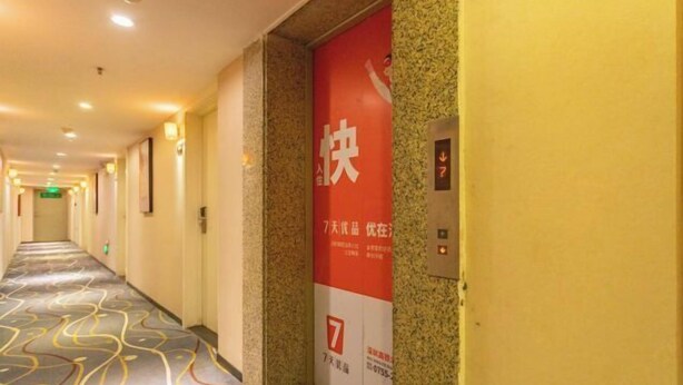 A hotel corridor with a patterned carpet, a red sign with white text, and an elevator control panel. - 7 Days Premium Hotel(Shenzhen North Station Yicheng Center Branch) (Shenzhen)
