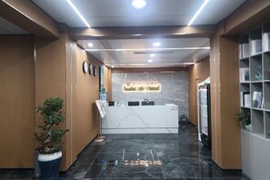 Un espace d’accueil avec un comptoir en marbre, un bureau de réception, une horloge et une plante en pot.