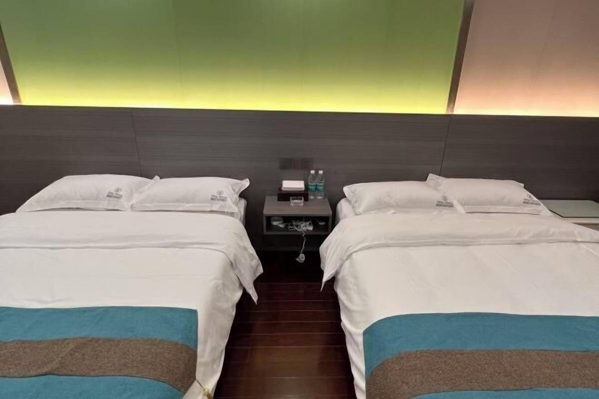 Habitación de hotel con dos camas, una mesita de noche con lámpara y una luz en la pared.