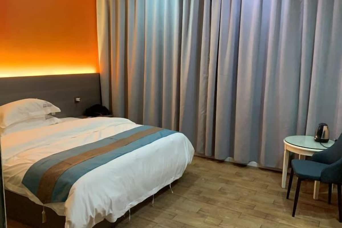 Una habitación de hotel con una cama, una mesita con hervidor y una silla.