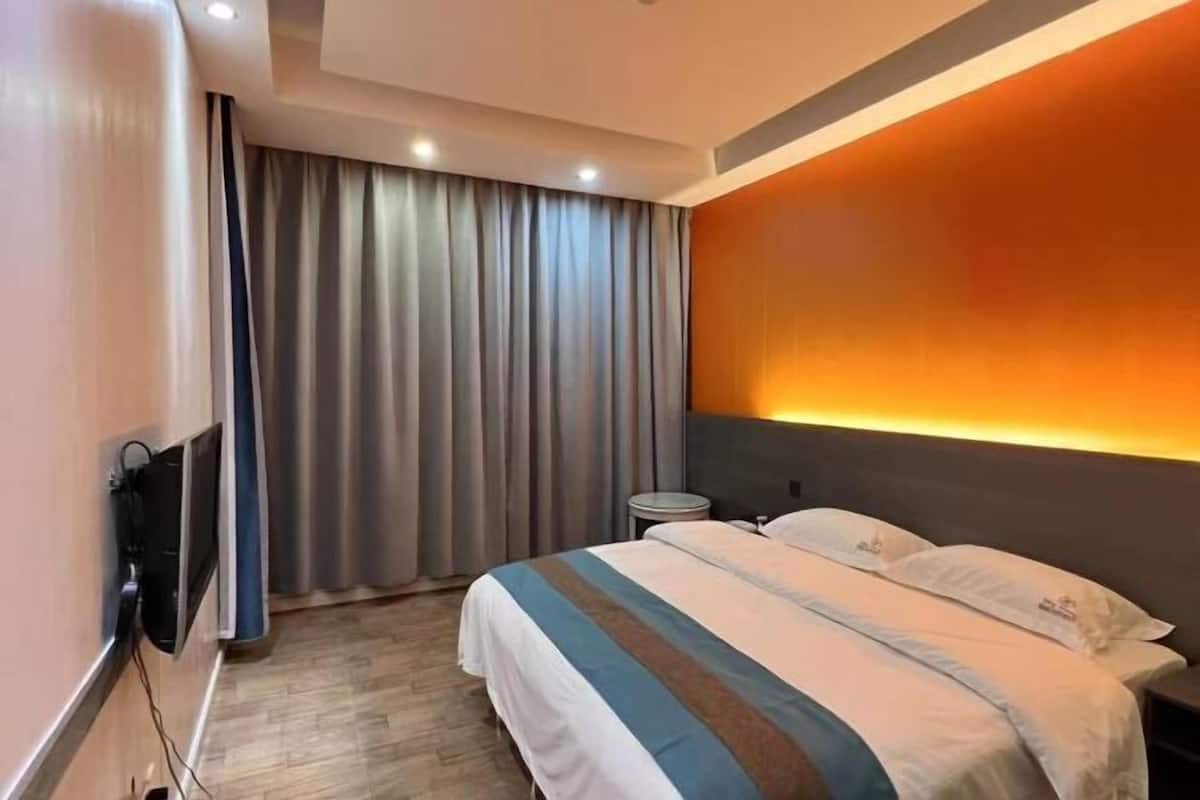 Una habitación de hotel con cama, cortinas, televisor montado en la pared y mesita de noche.