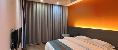 Une chambre d’hôtel avec un lit, des rideaux, un téléviseur fixé au mur et une table de chevet.