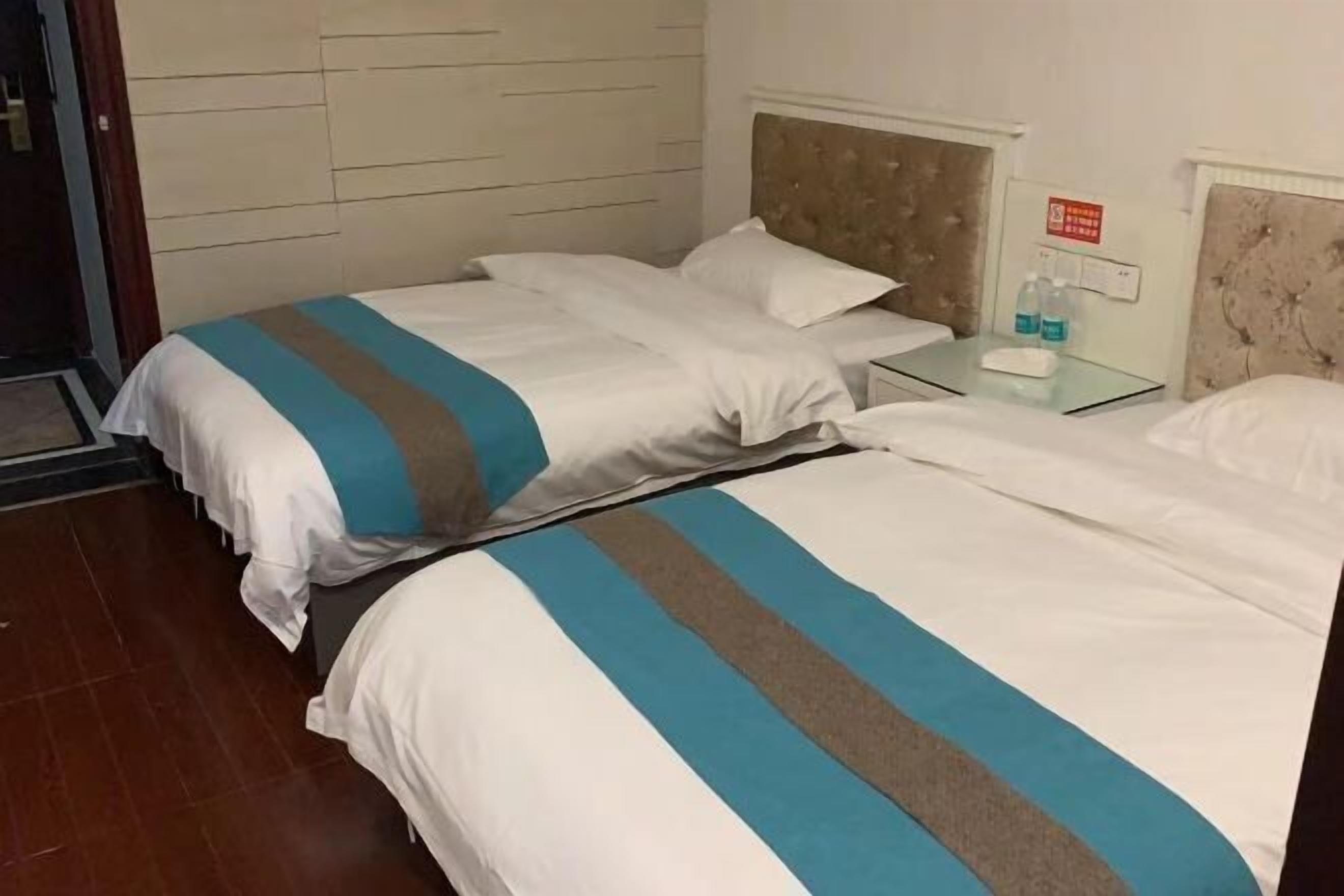 Habitación de hotel con dos camas, cada una con una colcha a rayas, una mesita de noche con una lámpara y un letrero en la pared.