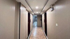 En hotellkorridor med ett kaklat golv, dörrar på båda sidor och en taklampa.