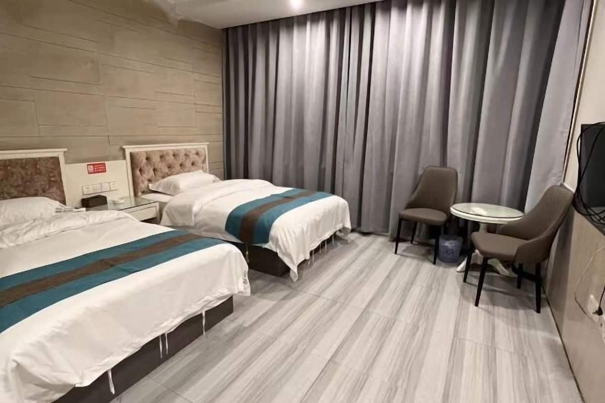 Habitación de hotel con dos camas, una mesita redonda y una silla.